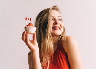 A happy woman in red holding a cupcake with a Canadian flag toothpick against a white background.