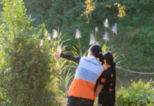 A humanitarian worker wearing a World Vision vest assists a child in a lush, sunny environment.