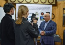 A journalist records an interview with a man using a camcorder indoors.