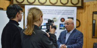 A journalist records an interview with a man using a camcorder indoors.