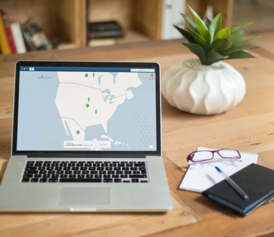 A laptop displaying VPN software sits on a wooden desk with a notepad and plant offering a secure workspace vibe.