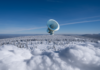 A large satellite dish observatory surrounded by snowy landscape and winter forest under a clear blue sky.