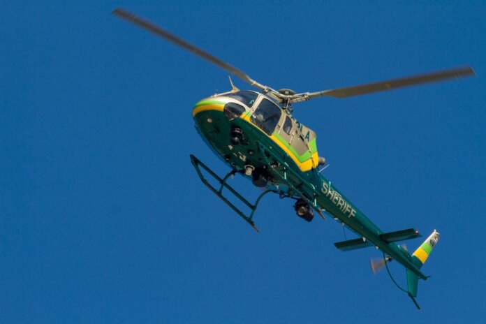 A Los Angeles County Sheriff helicopter soars through a clear blue sky.