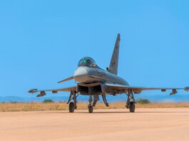 A military jet fighter on the runway ready for takeoff against a bright blue sky.