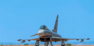 A military jet fighter on the runway ready for takeoff against a bright blue sky.