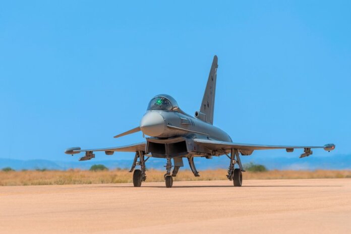 A military jet fighter on the runway ready for takeoff against a bright blue sky.