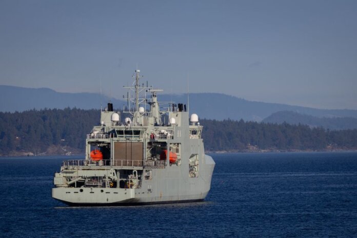 A military warship navigates through open waters with a coastline backdrop on a clear day. A military warship navigates through open waters with a coastline backdrop on a clear day.