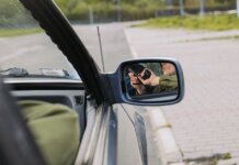 В Канаде перехвачено 392 украденных автомобиля на $28 млн A person with a gun captured in the car's side mirror, suggesting a mysterious scenario.