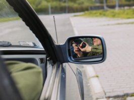 A person with a gun captured in the car's side mirror, suggesting a mysterious scenario.