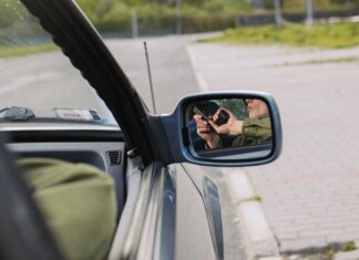 В Канаде перехвачено 392 украденных автомобиля на $28 млн A person with a gun captured in the car's side mirror, suggesting a mysterious scenario.