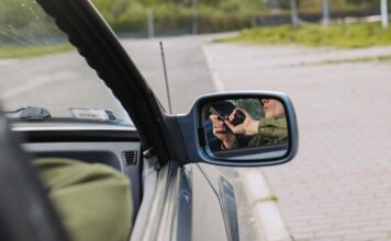 В Канаде перехвачено 392 украденных автомобиля на $28 млн A person with a gun captured in the car's side mirror, suggesting a mysterious scenario.