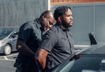 A police officer handcuffing a man next to a car in a parking lot.