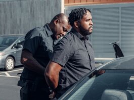 A police officer handcuffing a man next to a car in a parking lot.