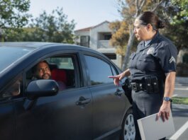 A police officer interacts with a driver during a daytime traffic stop on a residential street.