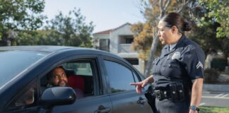 A police officer interacts with a driver during a daytime traffic stop on a residential street.