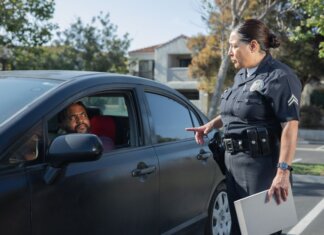 A police officer interacts with a driver during a daytime traffic stop on a residential street.