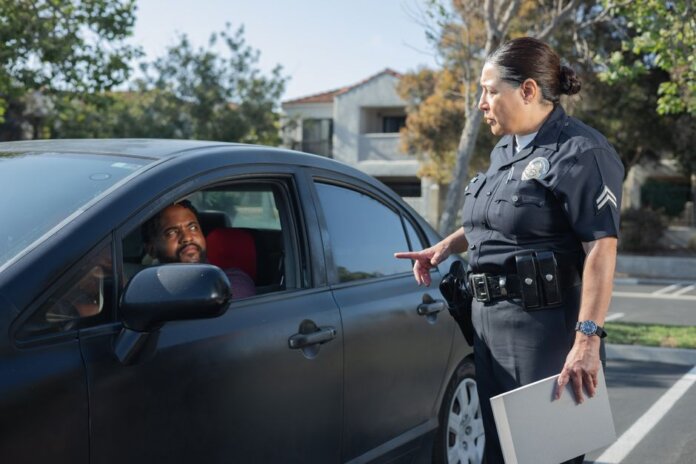 A police officer interacts with a driver during a daytime traffic stop on a residential street. A police officer interacts with a driver during a daytime traffic stop on a residential street.