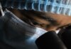 A scientist in protective gear intensely looking through a microscope.