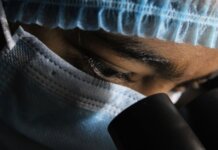 A scientist in protective gear intensely looking through a microscope.