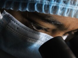 A scientist in protective gear intensely looking through a microscope.