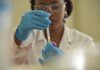 A scientist working with test tubes, wearing gloves and eyeglasses in a lab.