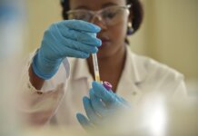 A scientist working with test tubes, wearing gloves and eyeglasses in a lab.