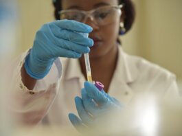 A scientist working with test tubes, wearing gloves and eyeglasses in a lab.