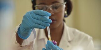 A scientist working with test tubes, wearing gloves and eyeglasses in a lab.