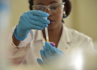 A scientist working with test tubes, wearing gloves and eyeglasses in a lab.