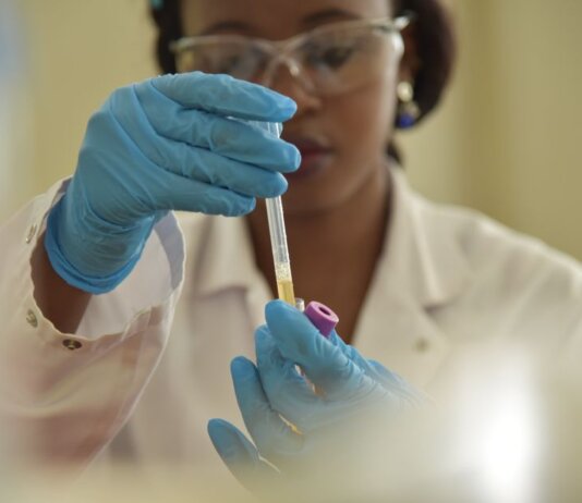 A scientist working with test tubes, wearing gloves and eyeglasses in a lab.