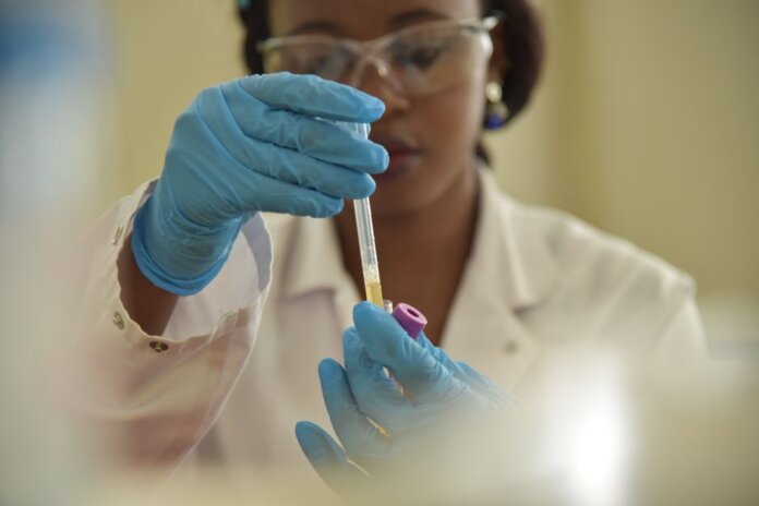 A scientist working with test tubes, wearing gloves and eyeglasses in a lab.
