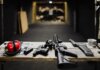 A selection of firearms and safety gear on a table at an indoor shooting range.