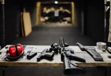 A selection of firearms and safety gear on a table at an indoor shooting range.