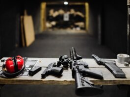 A selection of firearms and safety gear on a table at an indoor shooting range.