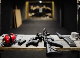 A selection of firearms and safety gear on a table at an indoor shooting range.