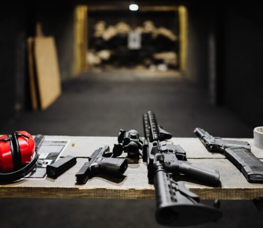 A selection of firearms and safety gear on a table at an indoor shooting range.