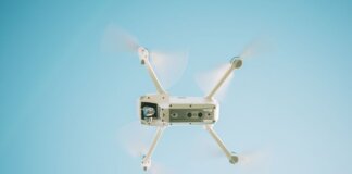 A sleek white drone flying under a clear blue sky, capturing aerial views.