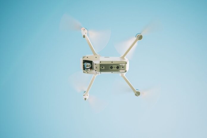 A sleek white drone flying under a clear blue sky, capturing aerial views.