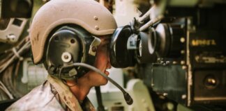 A soldier in uniform operates military equipment inside a vehicle, showcasing modern military technology.