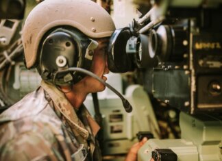 A soldier in uniform operates military equipment inside a vehicle, showcasing modern military technology.