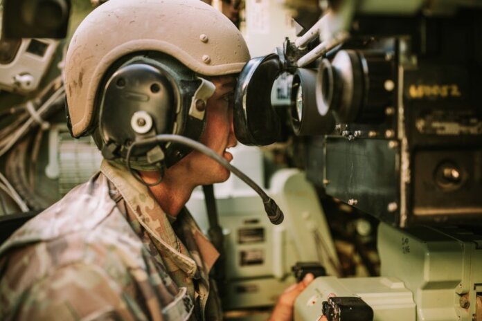 A soldier in uniform operates military equipment inside a vehicle, showcasing modern military technology.