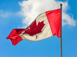 A vibrant Canadian flag waving against a blue sky with clouds.