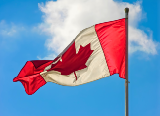 A vibrant Canadian flag waving against a blue sky with clouds.