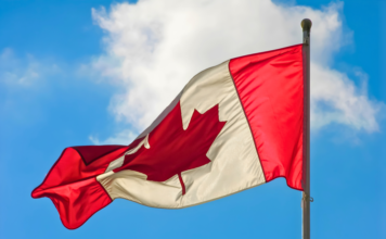 Правительство Канады поддержит возвращение фестиваля Taste of the Danforth A vibrant Canadian flag waving against a blue sky with clouds.