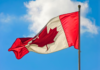 Правительство Канады поддержит Карибский карнавал в Торонто A vibrant Canadian flag waving against a blue sky with clouds.