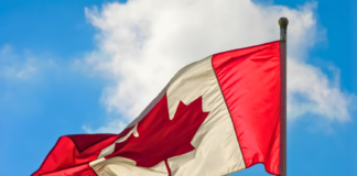 A vibrant Canadian flag waving against a blue sky with clouds.