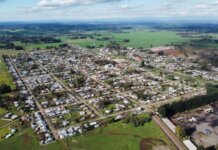 Aerial photo of a rural town surrounded by green fields under a cloudy sky, showcasing its layout.