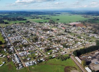 Aerial photo of a rural town surrounded by green fields under a cloudy sky, showcasing its layout.