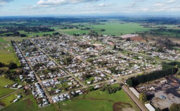 Aerial photo of a rural town surrounded by green fields under a cloudy sky, showcasing its layout.