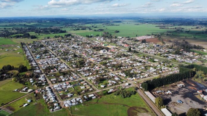 Aerial photo of a rural town surrounded by green fields under a cloudy sky, showcasing its layout. Aerial photo of a rural town surrounded by green fields under a cloudy sky, showcasing its layout.